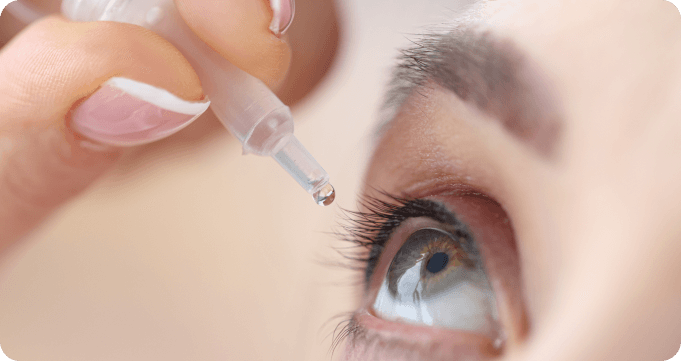 A close up of a woman applying eye drops to her eyes